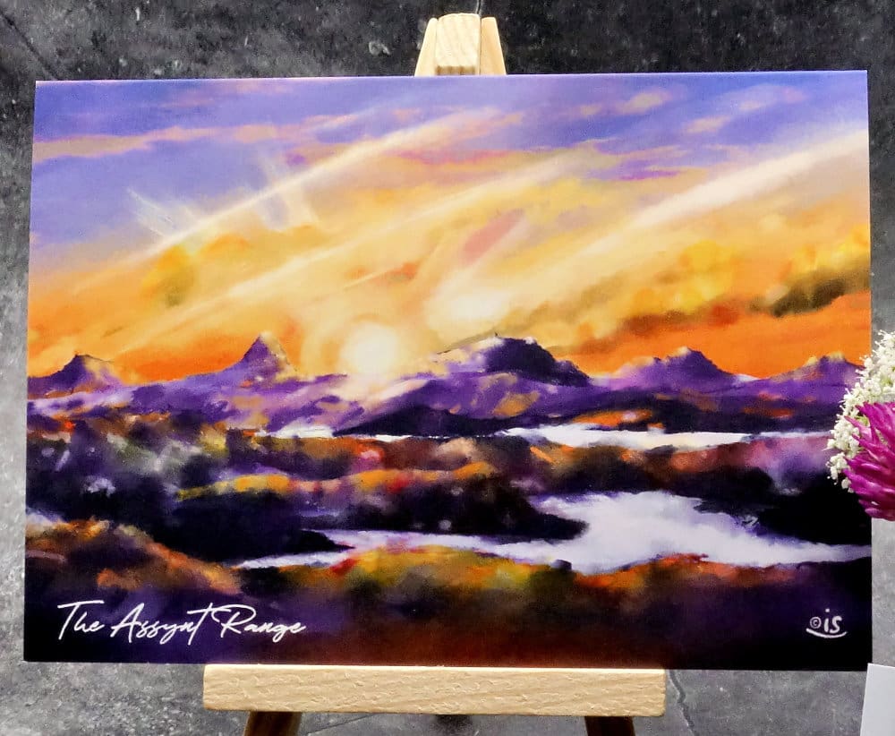 Larger image titled The Assynt Range showing an A6 size greetings card, blank inside, on a small easel depicting a view of the Assynt mountain range. From Left, Canisp, Suilven, Cul Mhor, Cul Beg and Stac Pollaidh - viewed from the North.