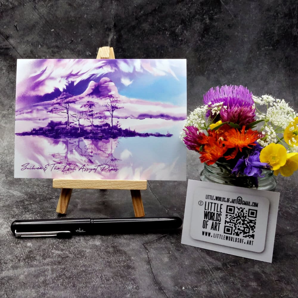 Image titled Loch Assynt Pines and Suilven showing an A6 size greetings card, blank inside, on a small easel depicting a view of old pine trees on islands on Loch Assynt, Sutherland in purple & blue watercolour.