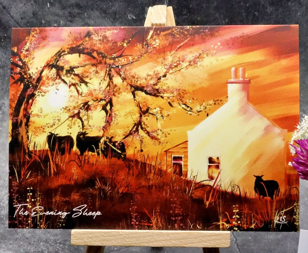 Larger image titled The Evening Sheep showing an A6 size greetings card, blank inside, on a small easel depicting a view of sheep in the croft garden on a warm summers evening during a vivid golden sunset.