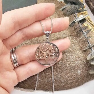 Artisan tree of life silver memorial circular pendant with ashes in clear resin beneath branches displayed in jeweller's hand