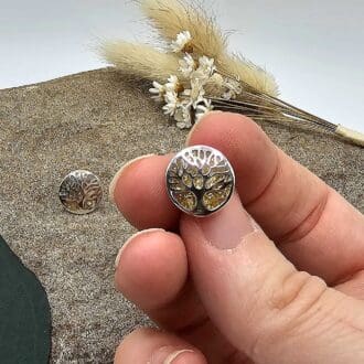 Jeweller showing handmade silver tree of life stud earring with gold-leaf resin keepsake displayed above a decorative stone