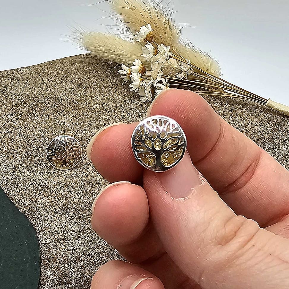 Jeweller showing handmade silver tree of life stud earring with gold-leaf resin keepsake displayed above a decorative stone