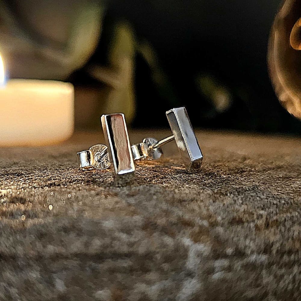 Pair of handcrafted rectangular solid sterling silver stud earrings displayed on decorative stone, in soft light