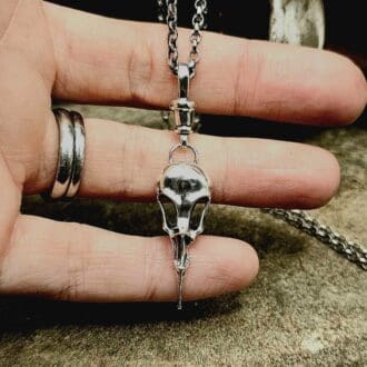 Handcrafted recycled sterling silver raven bird skull pendant with clasp displayed on jeweller's fingers and decorative stone