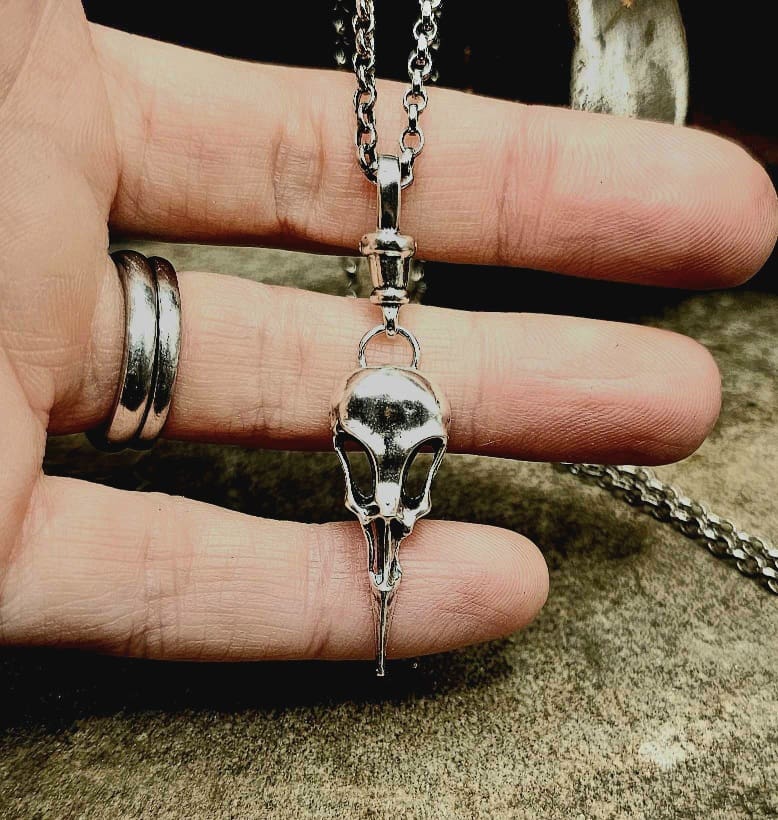 Handcrafted recycled sterling silver raven bird skull pendant with clasp displayed on jeweller's fingers and decorative stone