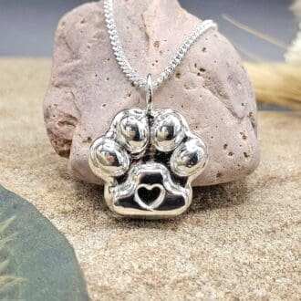 Handcrafted pet ashes into recycled sterling silver keepsake paw print shape pendant on chain displayed on decorative stone