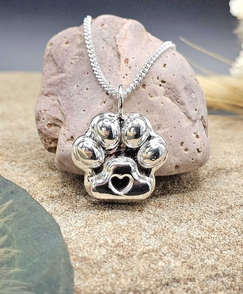 Handcrafted pet ashes into recycled sterling silver keepsake paw print shape pendant on chain displayed on decorative stone