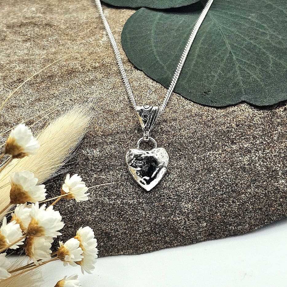 Displayed handmade sterling silver love heart pendant keepsake on silver chain with decorative stone background