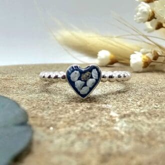 Handcrafted silver keepsake ring with memorial ashes in heart shaped deep blue resin setting displayed on stone with flowers