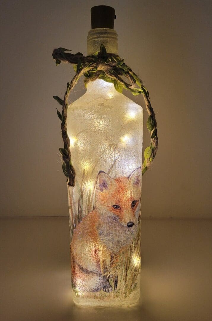 Lit up Square glass bottle with fox detail and green leafy jute twine around the neck. Cork LED lights