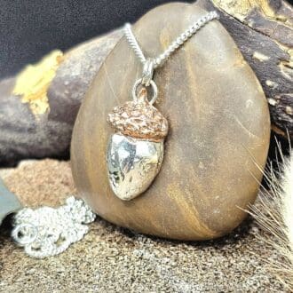 Handcrafted sterling silver and copper acorn keepsake pendant necklace on silver chain displayed on decorative pebble