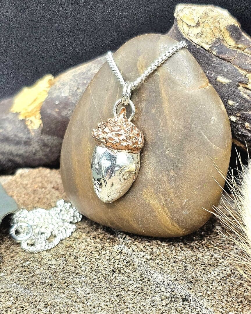 Handcrafted sterling silver and copper acorn keepsake pendant necklace on silver chain displayed on decorative pebble