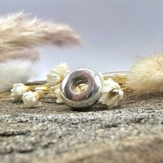 Handmade ashes into sterling silver universal round charm bead displayed on decorative pastel stone and small white flowers