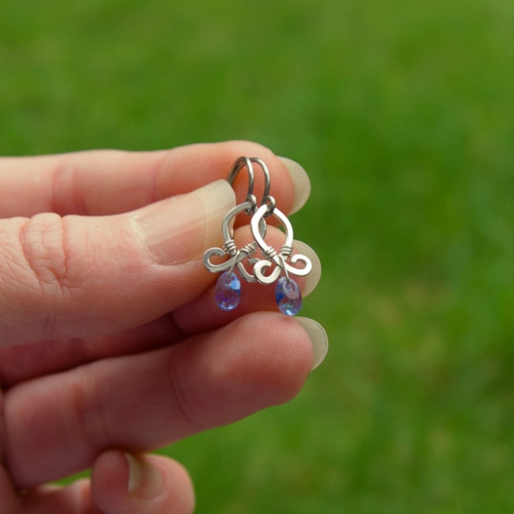 Hand holding a pair of small silver dangle earrings with blue beads by Oruki Design