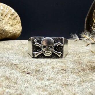 Handcrafted recycled sterling silver skull and crossbones jolly roger pirate flag signet ring displayed on decorative stone