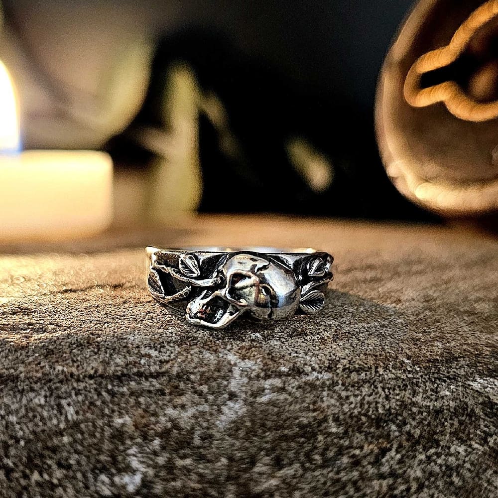 Handcrafted, skull and vine memento mori hallmarked silver ring displayed on decorative stone in soft candle light