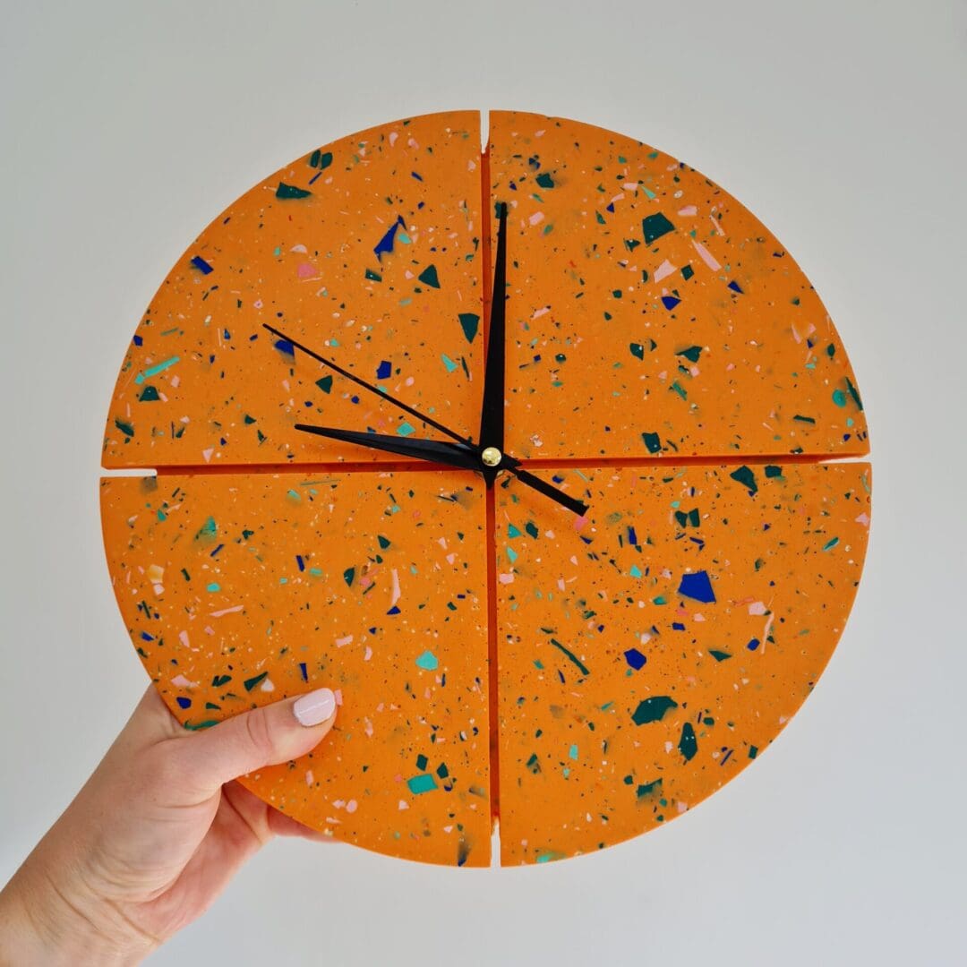 Round hanging wall clock featuring an orange base with rainbow terrazzo coloured chips