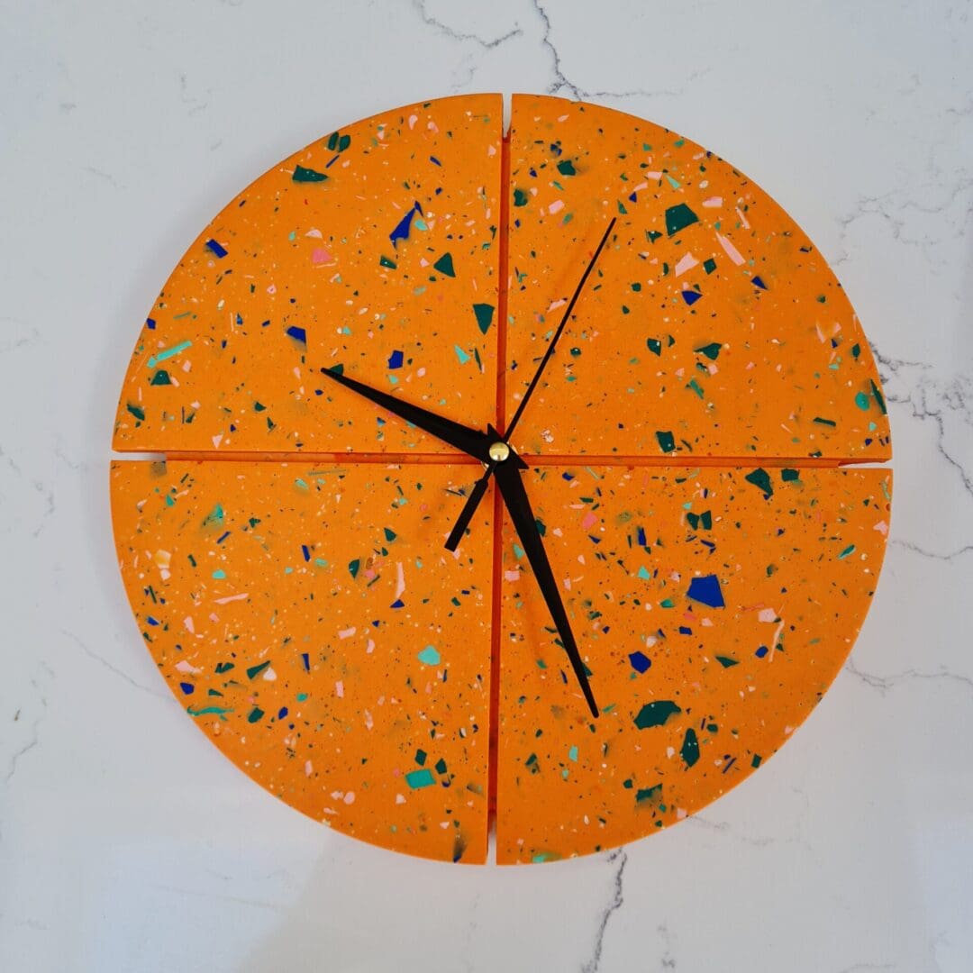 Round hanging wall clock featuring an orange base with rainbow terrazzo coloured chips