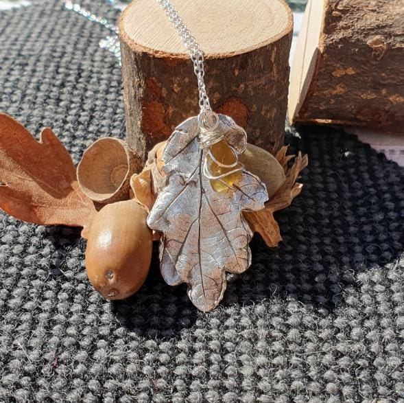 silver oak leaf with a honey amber sea glass charm hanging from a chain and displayed with a real oak leaf and acorn