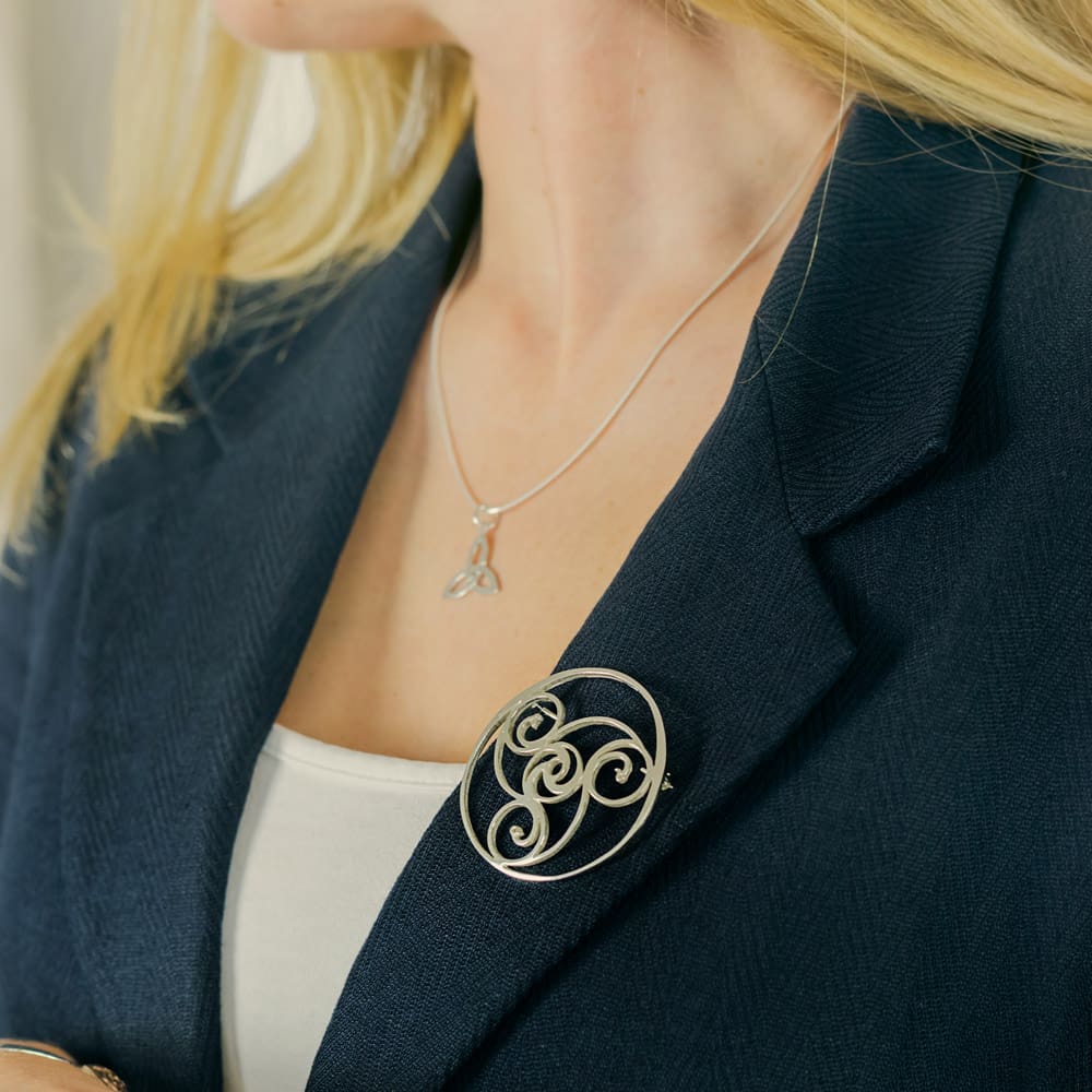 a model is showing the sterling silver brooch on the lapel of her dark blue green jacket. The brooch stands out beautifully against the dark background.