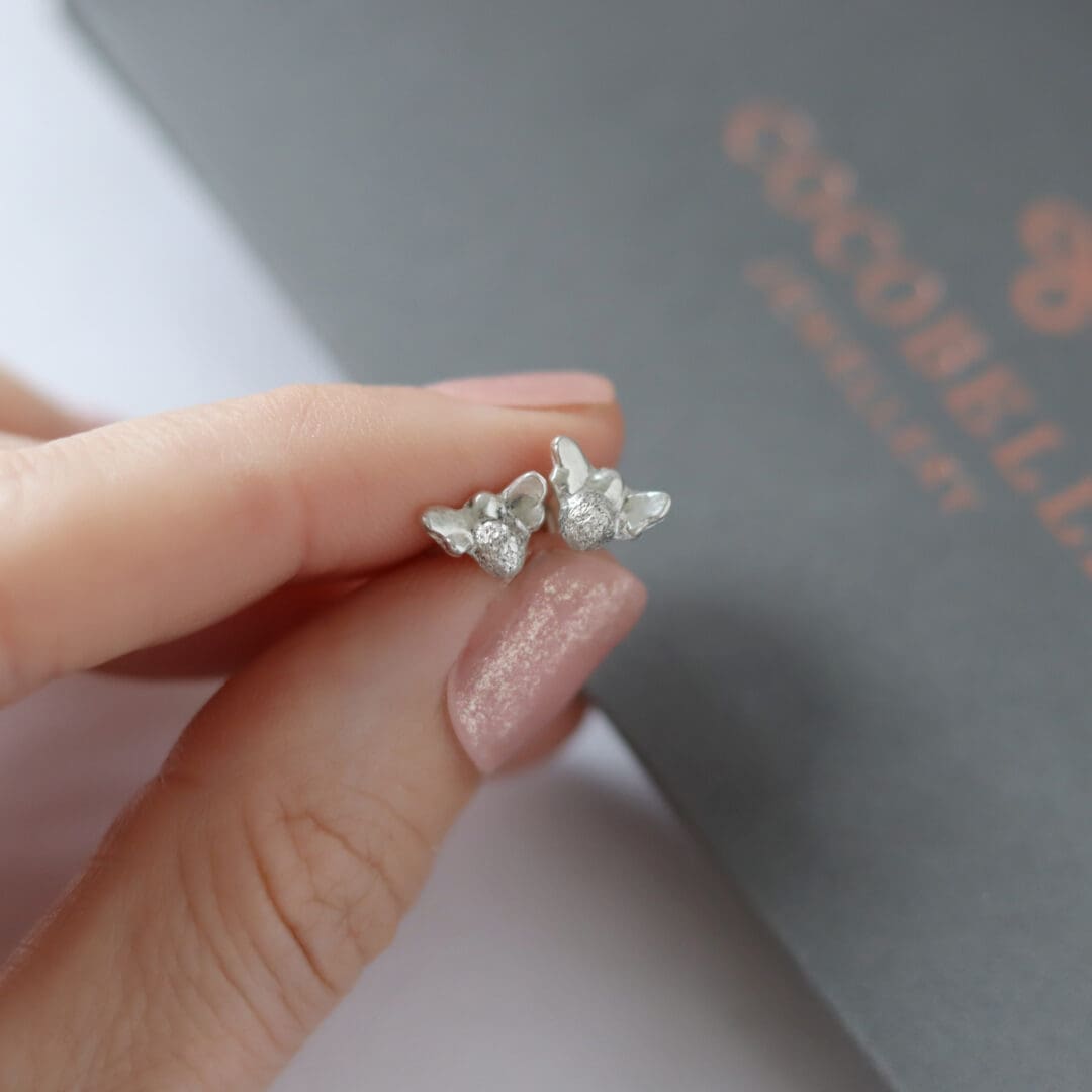 Silver bee stud earrings being held in front of a Cocobelle branded box