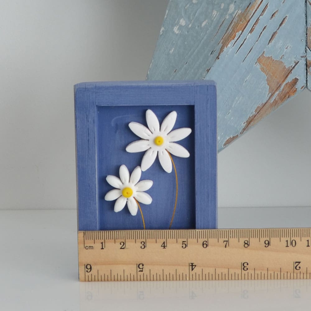 Miniature handmade wooden open frame in a distressed blue chalk paint with two small clay daisy flowers