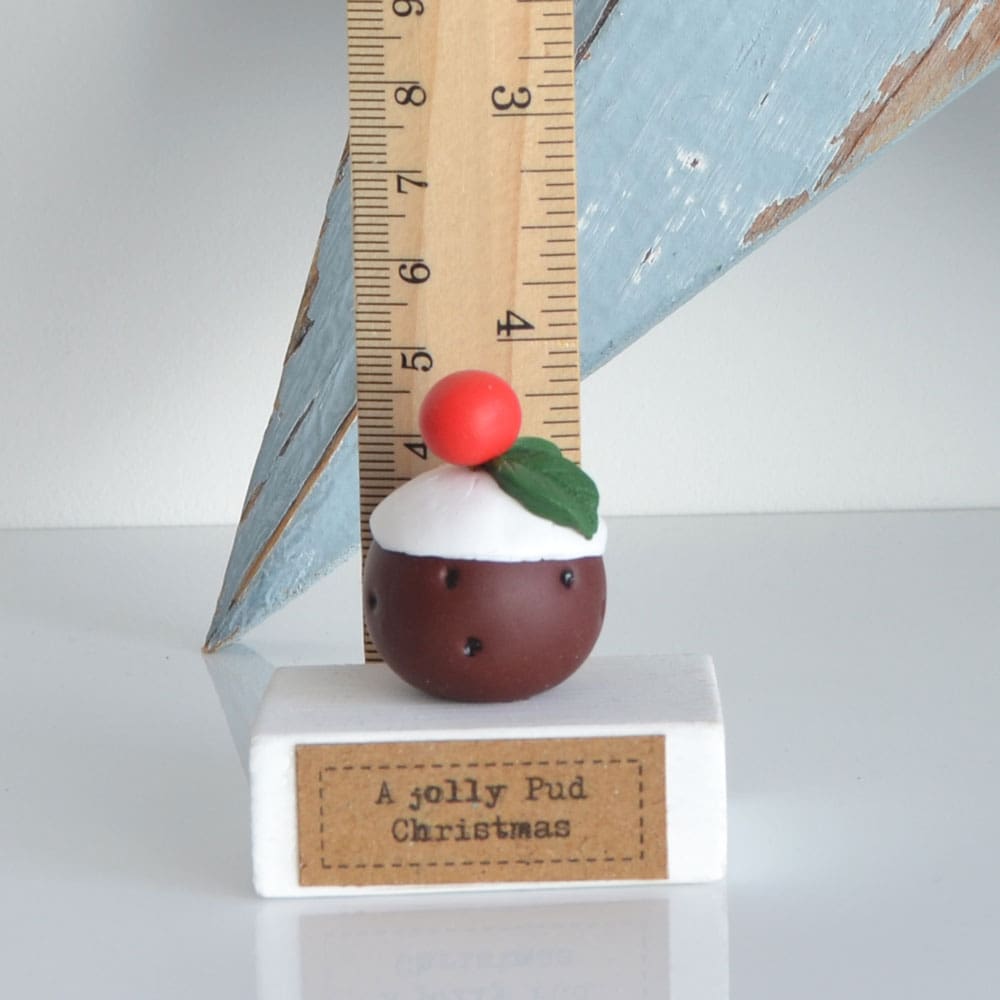 Clay Christmas Pudding ornament set on a white wooden base with the pun 'A Jolly Pud Christmas.