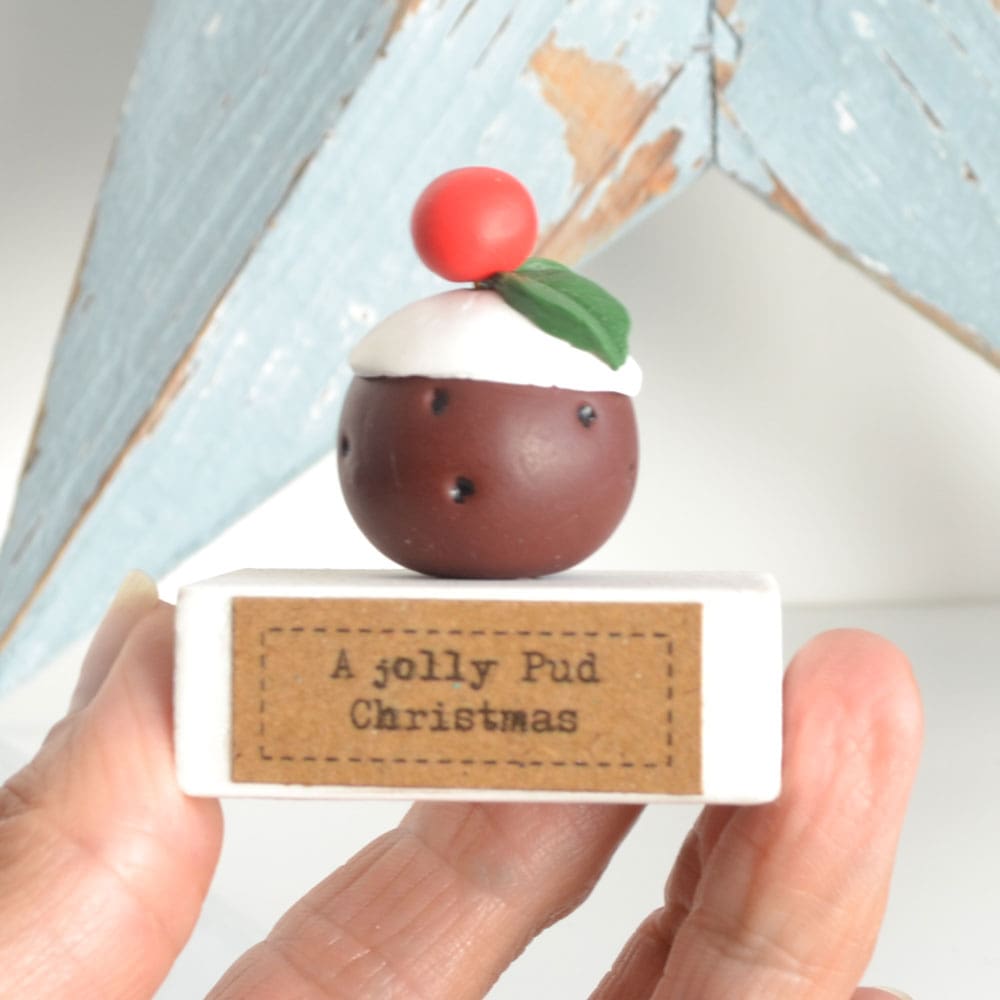 Clay Christmas Pudding ornament set on a white wooden base with the pun 'A Jolly Pud Christmas.