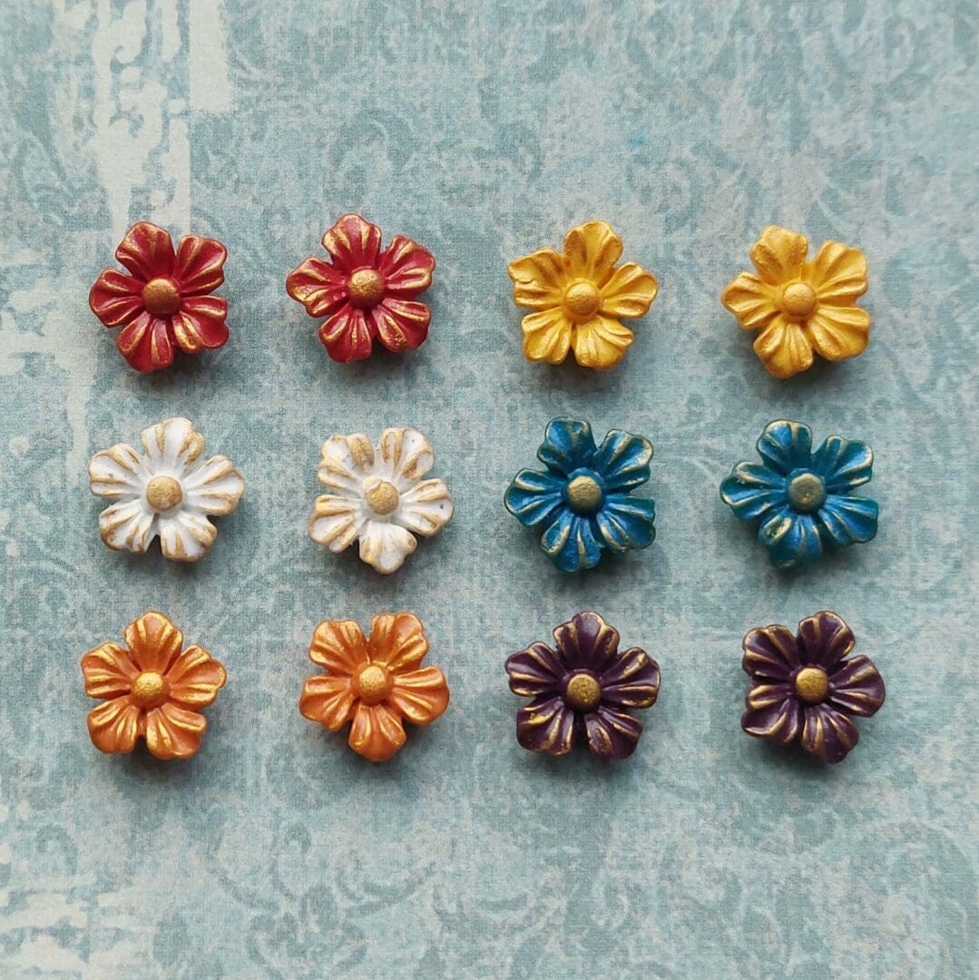 A collection of small handmade polymer clay flower stud earrings in Blue, red, orange, yellow, white and purple with gold details.