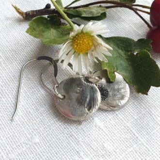 A daisy flower with a pair of silver circular earrings with daisy imprints