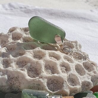 a green sea glass pendant resting on a lump of fossil coral with the light shining through