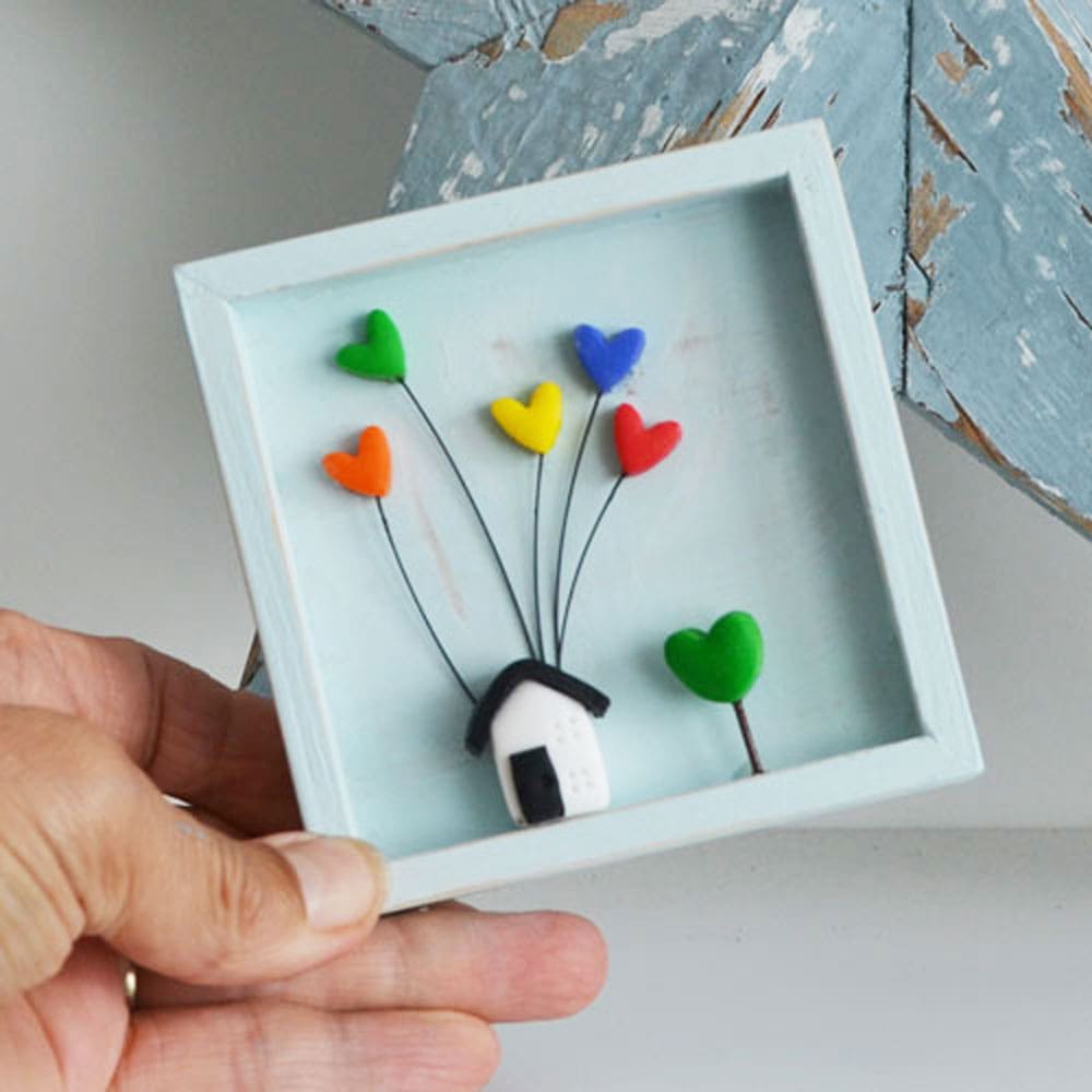 A miniature wooden frame with a rustic or distressed finish with a small clay house and rainbow hearts.