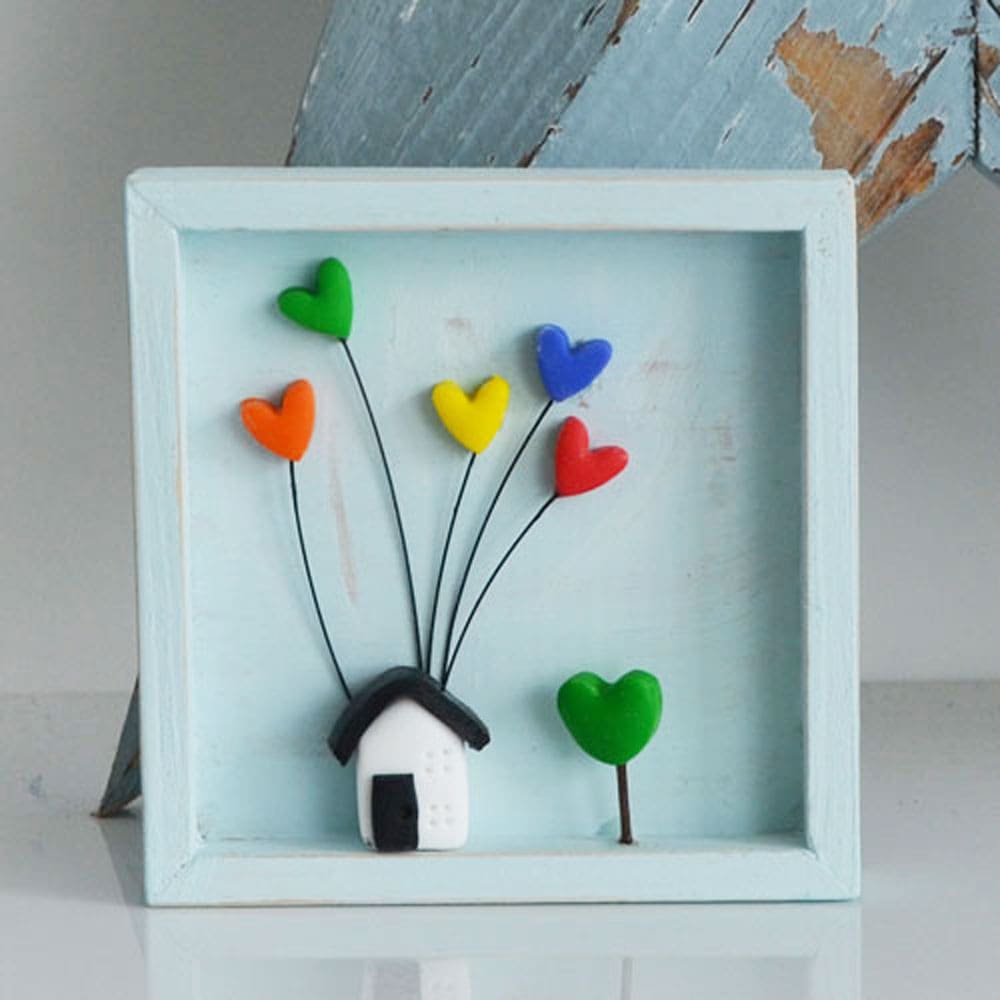 A miniature wooden frame with a rustic or distressed finish with a small clay house and rainbow hearts.