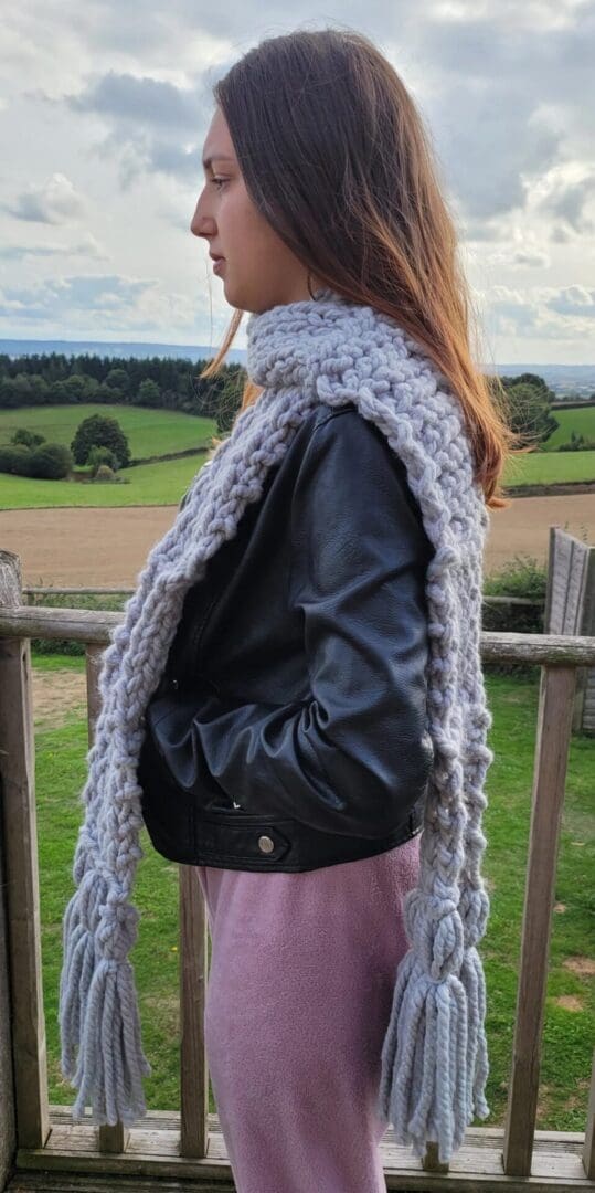 grey chunky knit scarf seen from the side, around the neck of model. Ends reach the knees