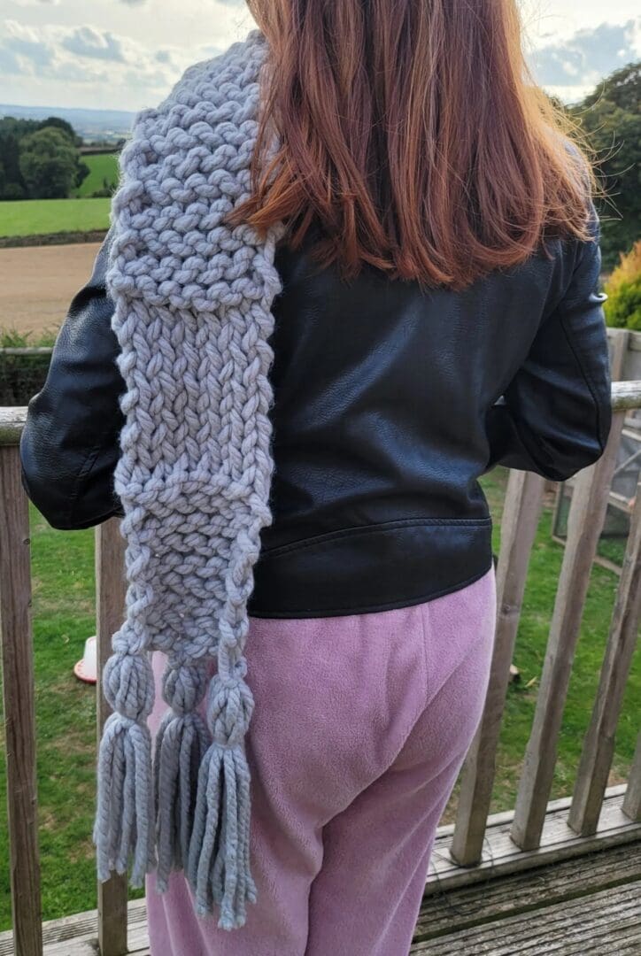 grey chunky knit scarf seen on a model. Scarf reached knees. Large tassels on scarf