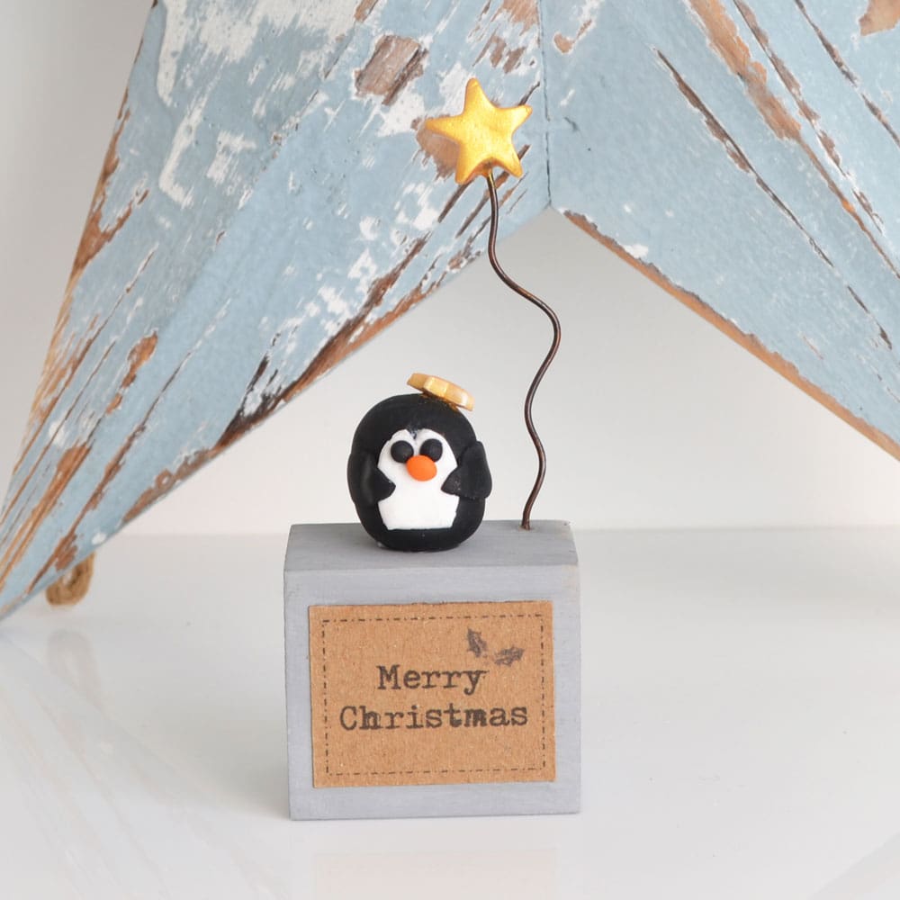 Handmade Merry Christmas decoration with grey wood base and clay penguin with gold star on wire.