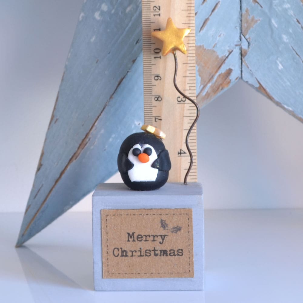 Handmade Merry Christmas decoration with grey wood base and clay penguin with gold star on wire.