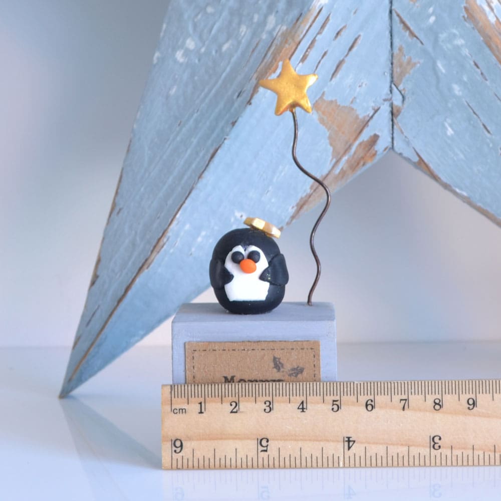 Handmade Merry Christmas decoration with grey wood base and clay penguin with gold star on wire.