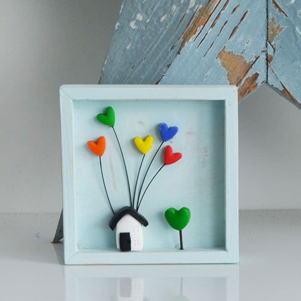 A miniature wooden frame with a rustic or distressed finish with a small clay house and rainbow hearts.