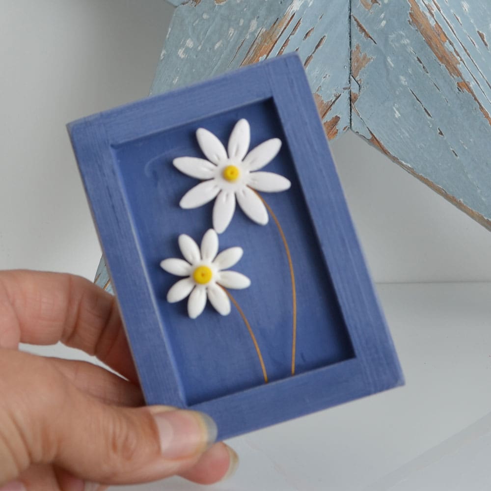 Miniature handmade wooden open frame in a distressed blue chalk paint with two small clay daisy flowers