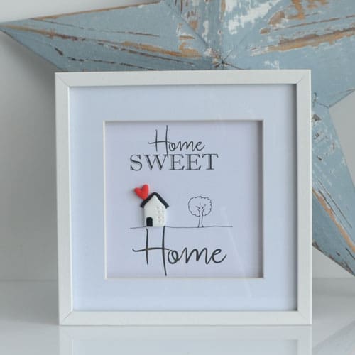 White frame with a Home Sweet Home sign inside and a little clay house with heart and a hand drawn tree.