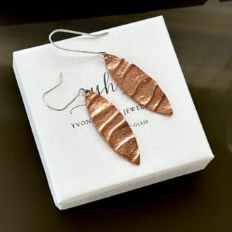 Copper leaf shaped drop earrings with sterling silver ear wires, sat on a small white gift box.