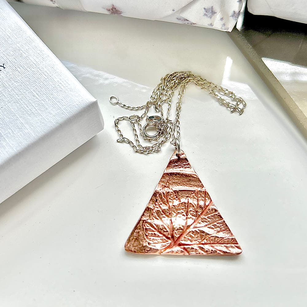 A triangle shaped copper pendant with a sterling silver chain. Displayed on a white background.