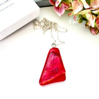 A red fused glass pendant with dichroic glass and a sterling silver bail and chain. Displayed on a white background.