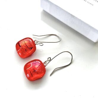 Red fused dichroic glass earrings with sterling silver ear wires. Displayed on a white surface with a white gift box.