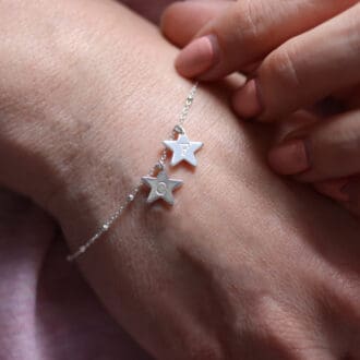 Close up of a wrist with a silver bracelet. The bracelet has 2 silver star charms. One has an engraved 'C' and one has an engraved 'F'