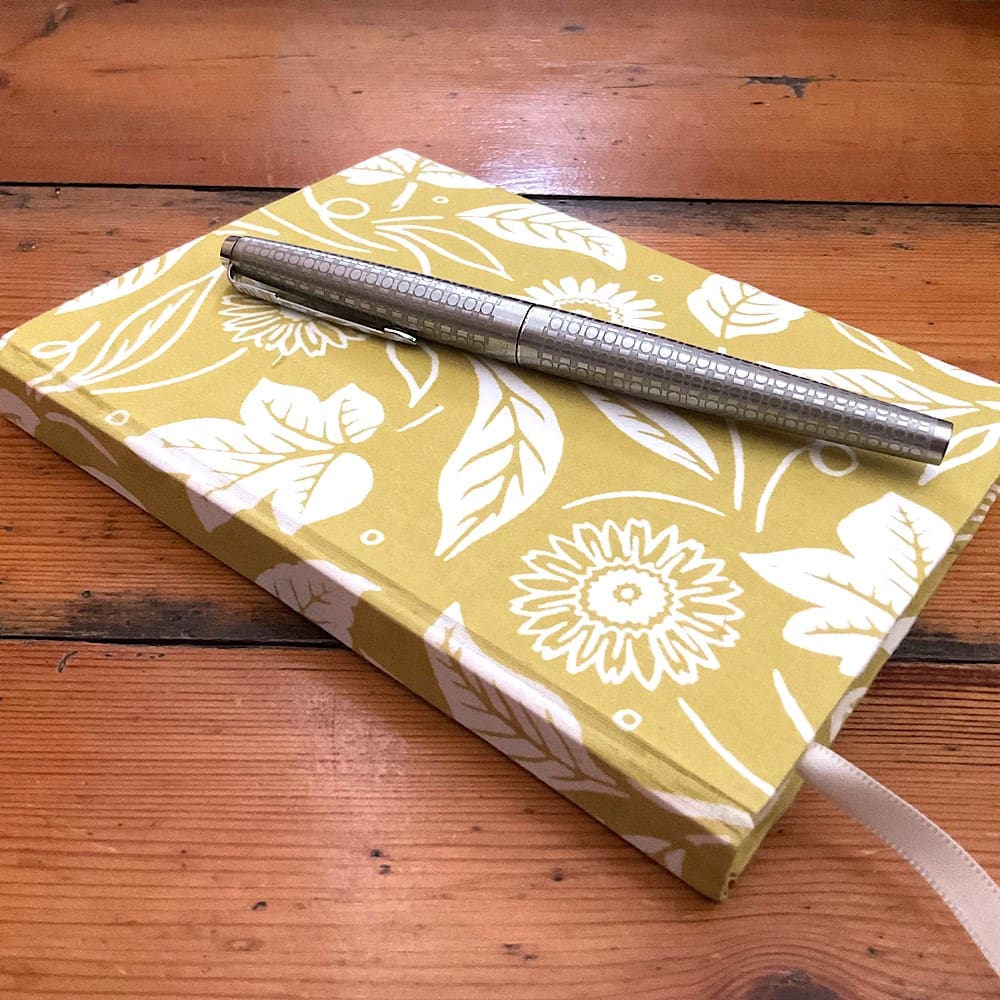 A6 lined paper handmade notebook covered in a mustard colour floral fabric