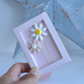 Miniature handmade wooden open frame in a distressed pink with two small clay daisy flowers in white and pink