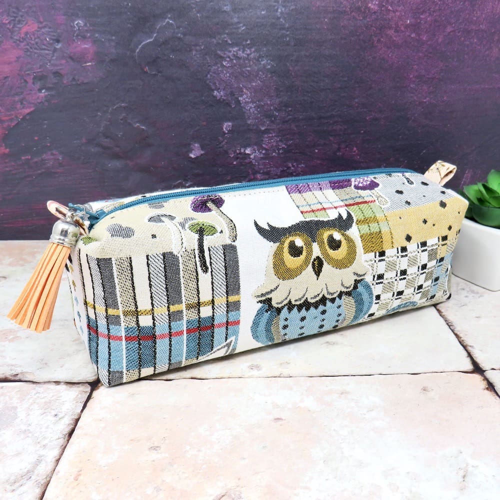 A zipped pencil case in an owl fabric with a faux suede zip pull.