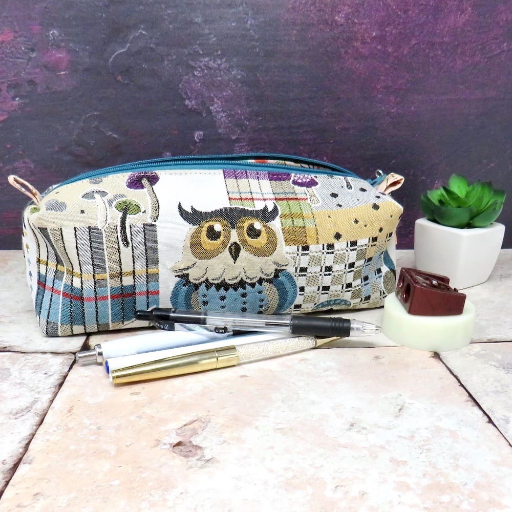 A zipped pencil case in an owl fabric with a faux suede zip pull.